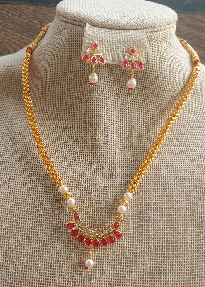 Elegant gold necklace and earrings set with ruby gemstones and lustrous pearls, displayed on a white textured jewelry stand.