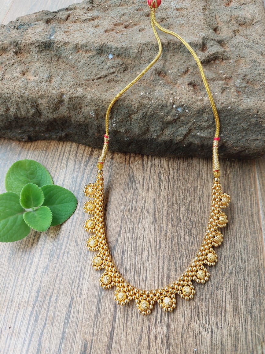 Ornate gold necklace with intricate, textured beads and accents displayed on a wooden surface with a shamrock-shaped leaf.