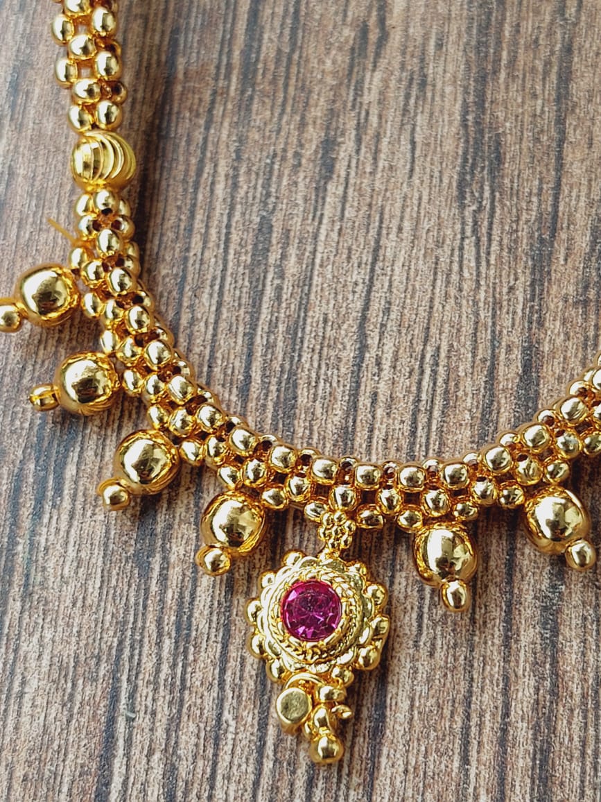 Elegant gold beaded necklace with decorative pink gemstone pendant, displayed on a rustic wooden surface.