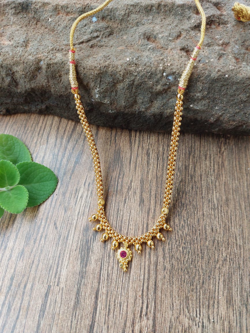Small golden floral bead thushi necklace with intricate detailing displayed on a wooden surface with a leaf in the background.