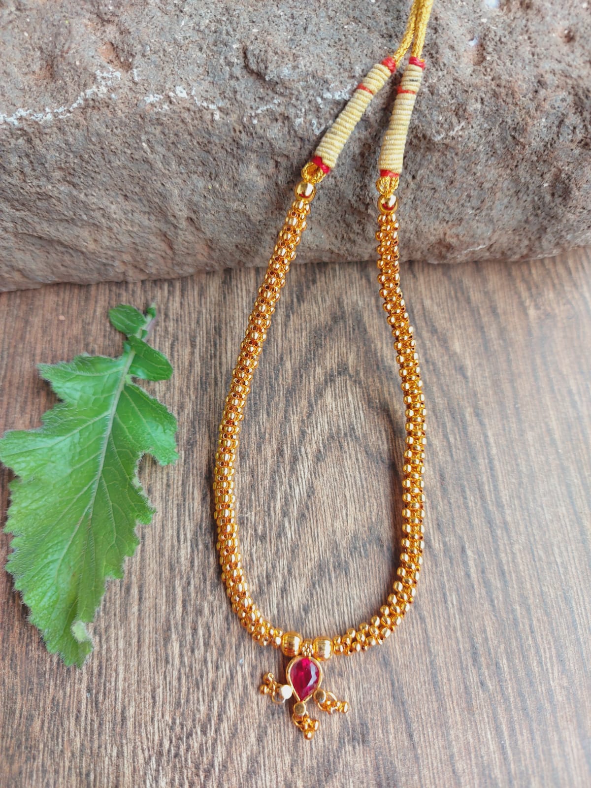 Traditional Red Stone Thushi Necklace with Golden Beads and Pendant on Wooden Background