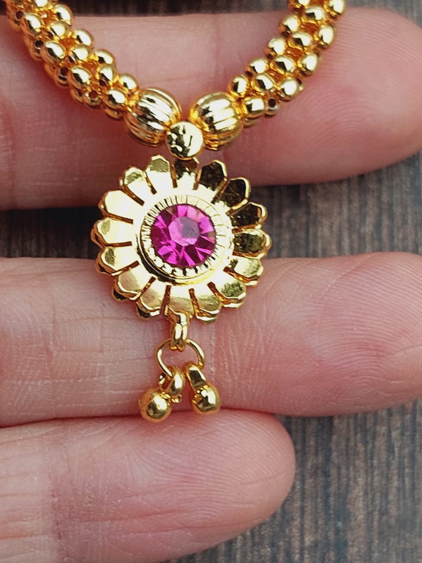Captivating golden floral necklace with vibrant pink gemstone pendant, showcased on a wooden surface.