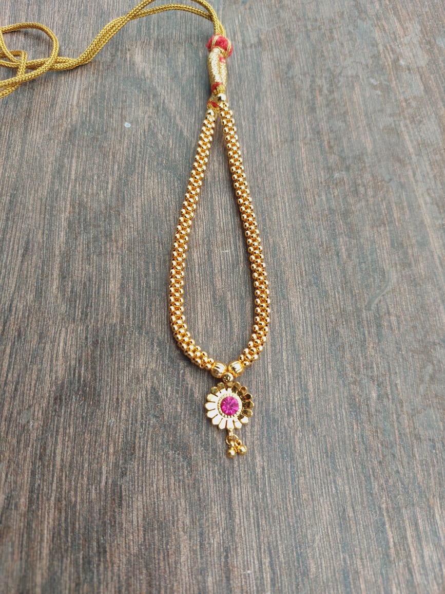 Gold-toned traditional necklace with a large red flower-shaped pendant adorned with crystals, displayed on a wooden surface.