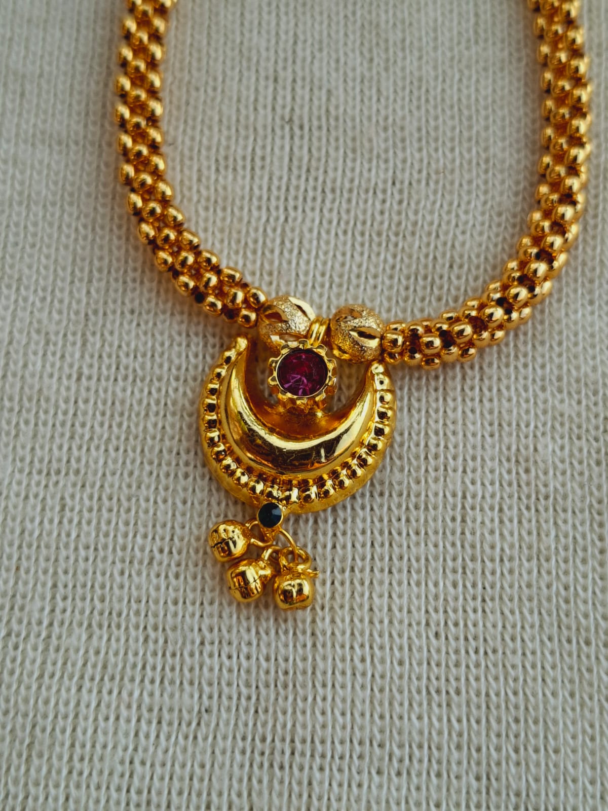 Chandrakor Thushi: Elegant gold-toned necklace with intricate pendant featuring ornate design and sparkling purple gem