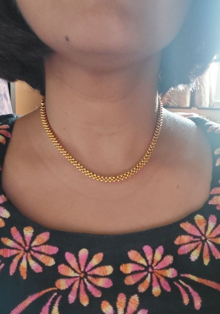 Elegant gold necklace with intricate chain design, complementing the floral patterned clothing in the image.