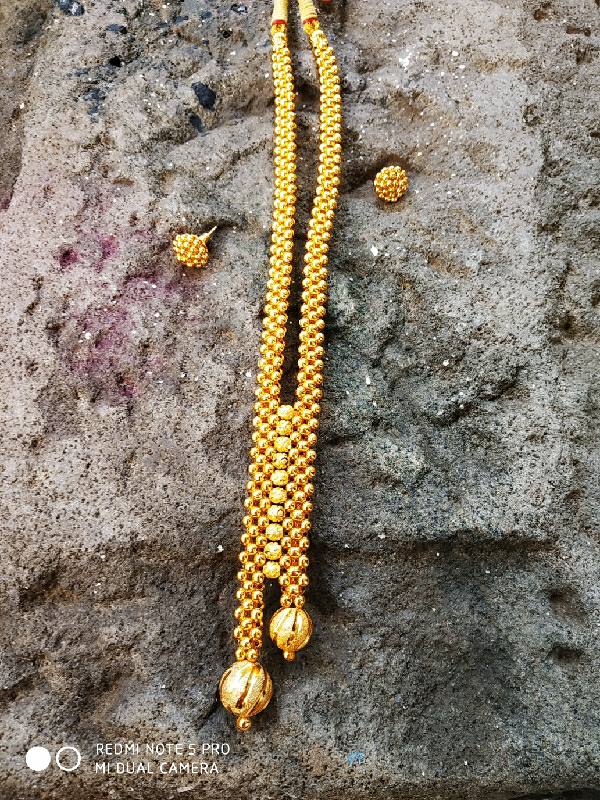 Elegant golden necklace with beaded strands and pendant drops, showcased on a textured rock surface.