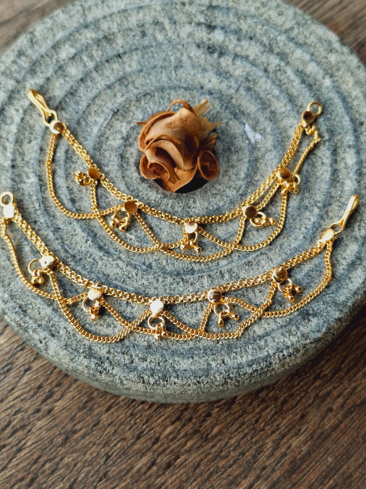 Designer golden ear chain with intricate floral and chain motifs on a gray textured background.