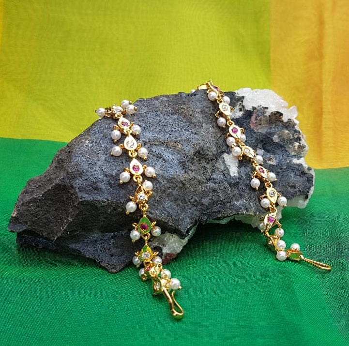 Elegant red and white AD pearl jewelry set with intricate gold-toned design, displayed on a rugged gray rock against a vibrant green and yellow background.