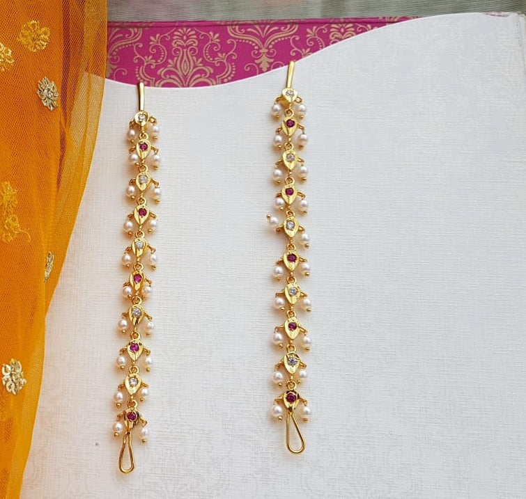 Elegant gold-toned AD pearl wel accessory with intricate floral design, displayed against a vibrant pink and orange backdrop in the Mugdha Jewellery Store.