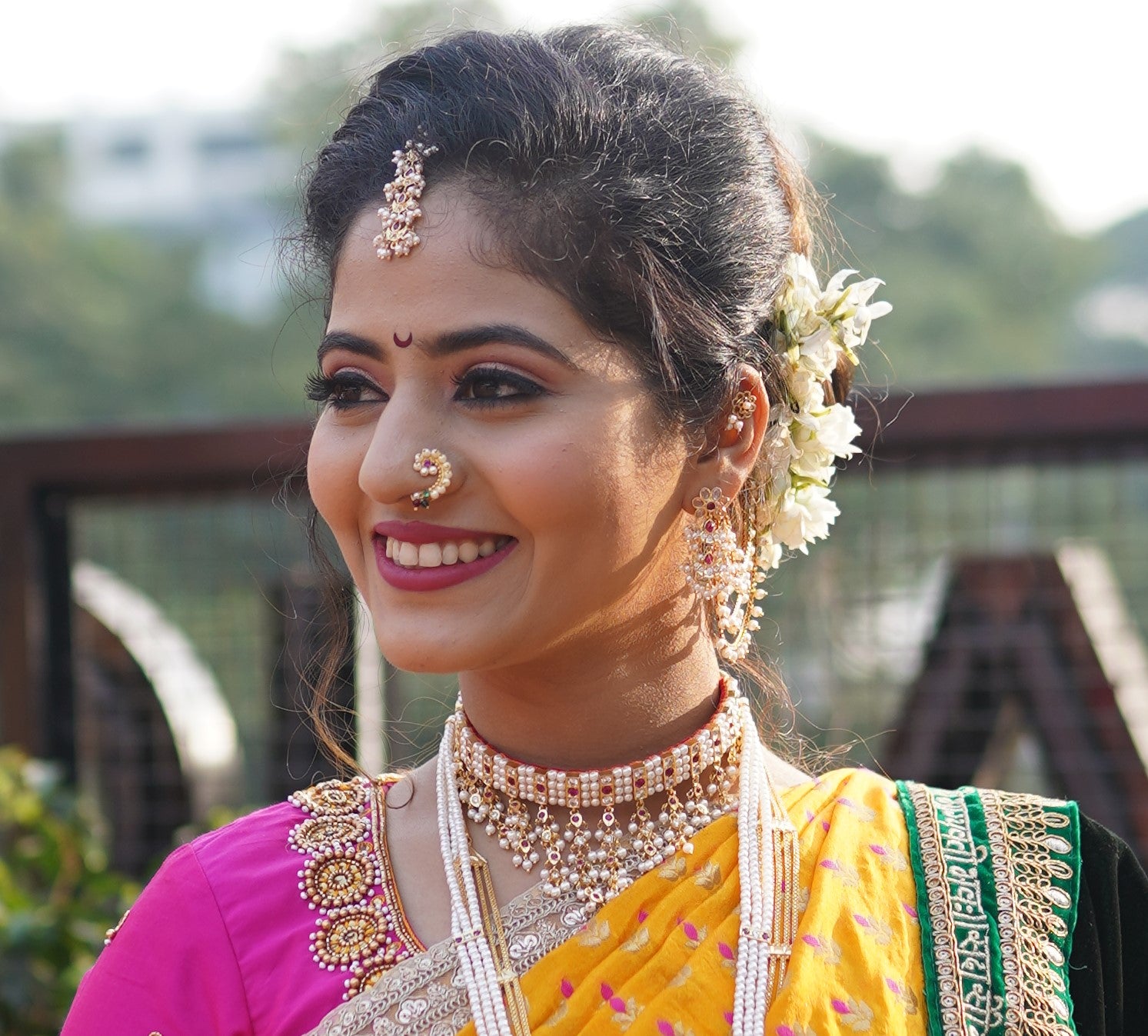 Dark pink, white, and gold traditional Indian jewelry adorning a smiling woman in a yellow and magenta outfit.