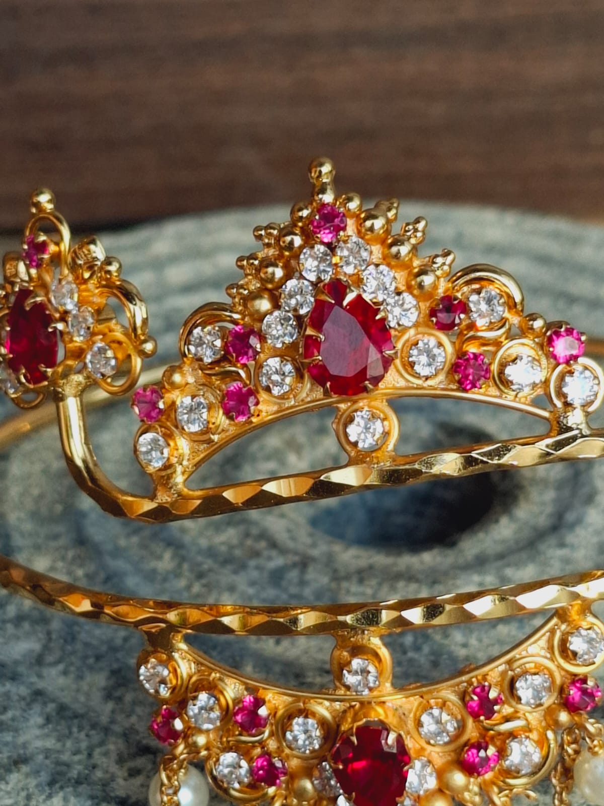 Ornate gold-toned tiara adorned with sparkling red and clear gemstones, placed on a dark surface.