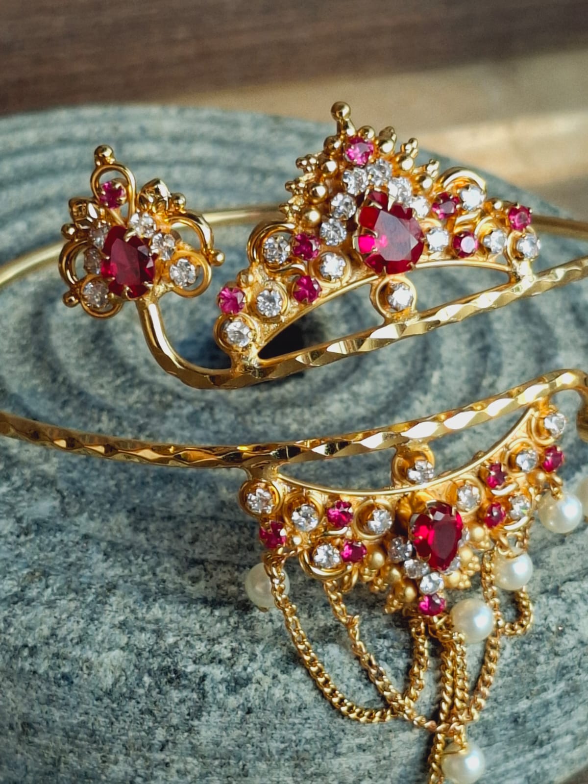 Ornate golden bajuband with sparkling ruby and diamond embellishments on a stone backdrop in the Mugdha Jewellery Store.