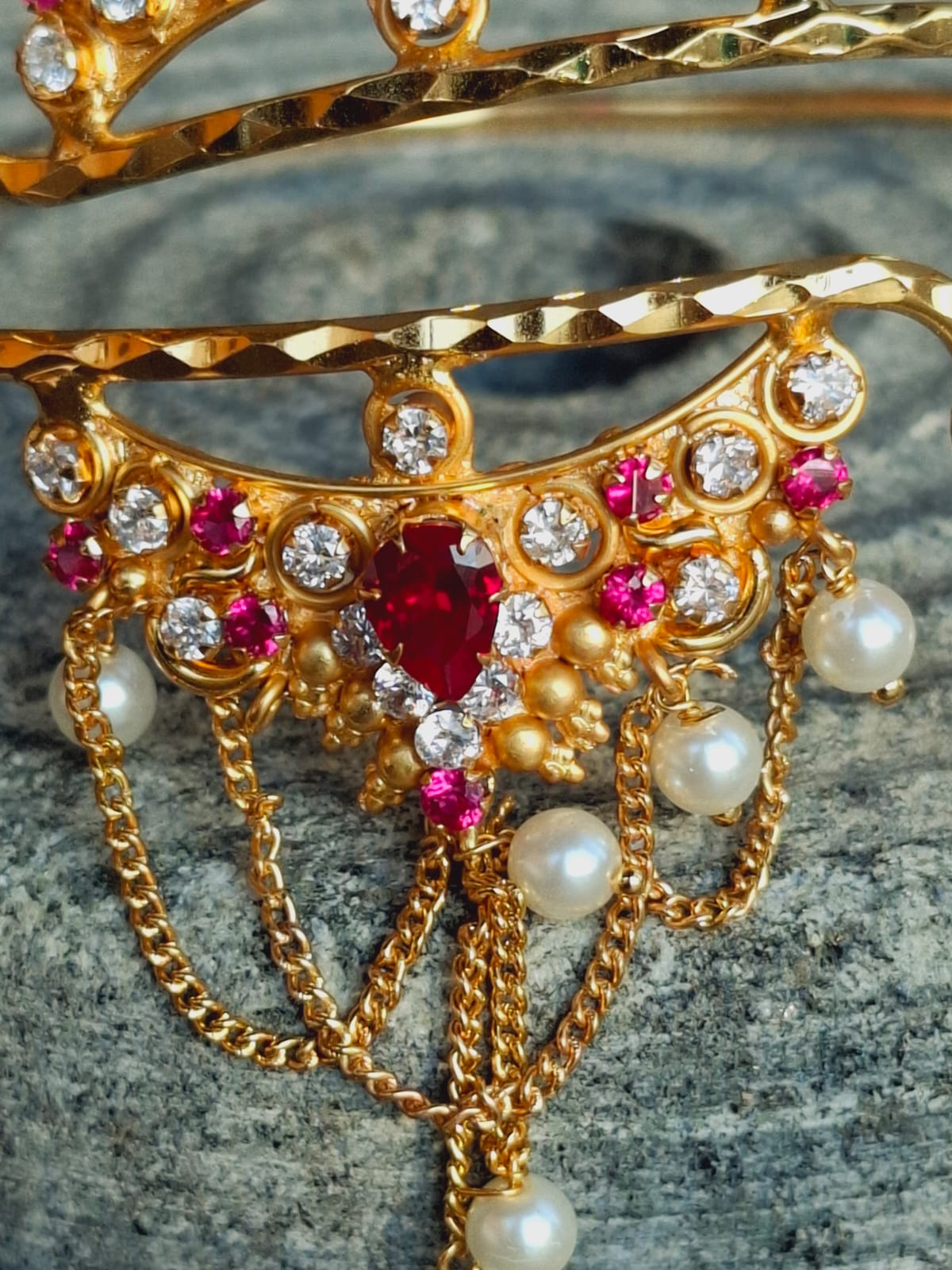 Intricate golden bajuband adorned with vibrant rubies, sparkling diamonds, and lustrous pearls displayed on a textured surface.