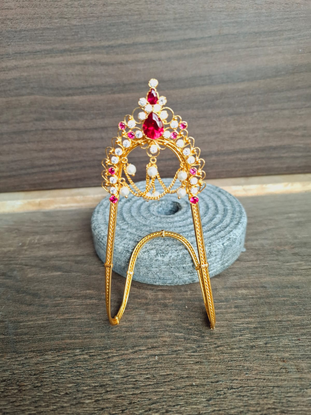 Elegant gold-toned arm cuff adorned with vibrant gemstones, placed on a grey satin cushion.