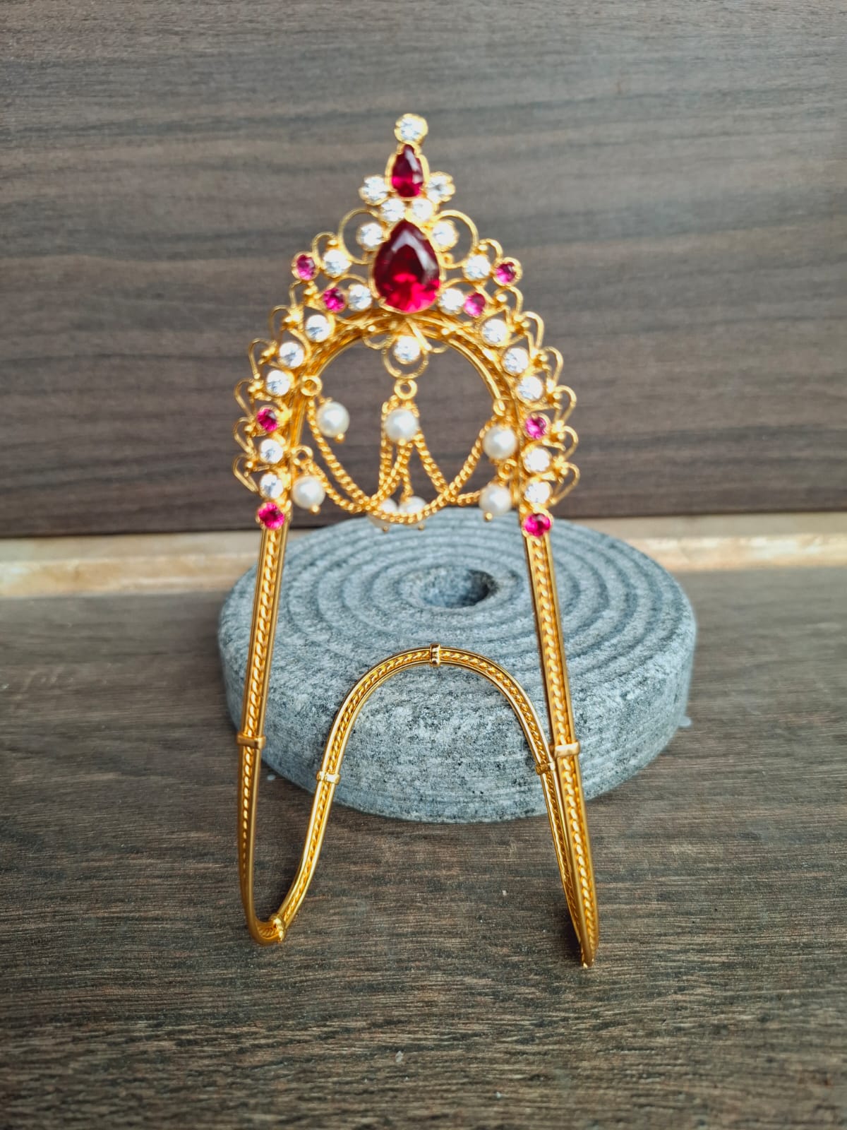 Bejeweled gold-toned crown with vibrant red and yellow gemstones, placed on a gray cloth surface.