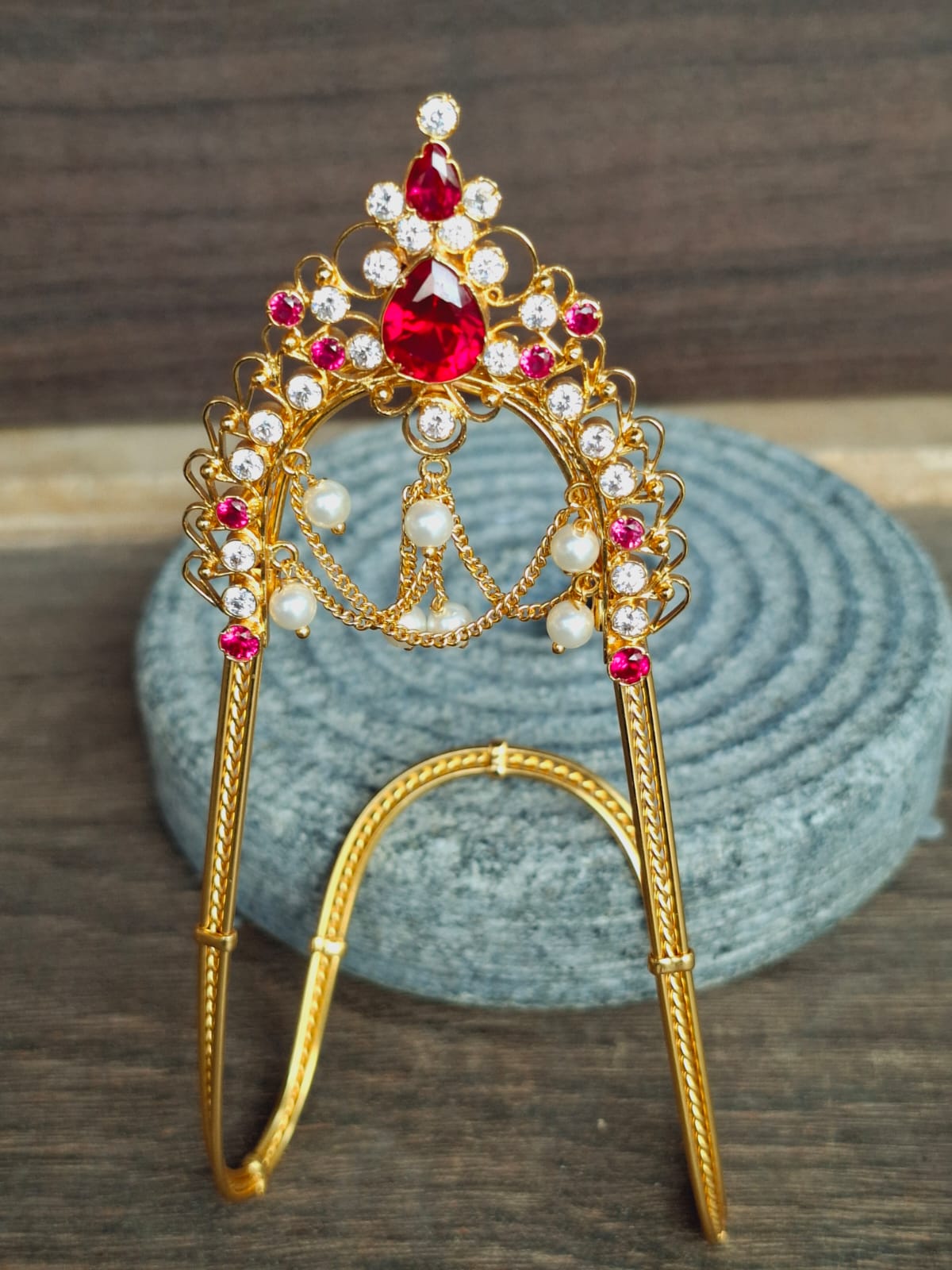 Elegant gold-toned bajubandh decorated with sparkling red and white gemstones, displayed on a textured gray surface.