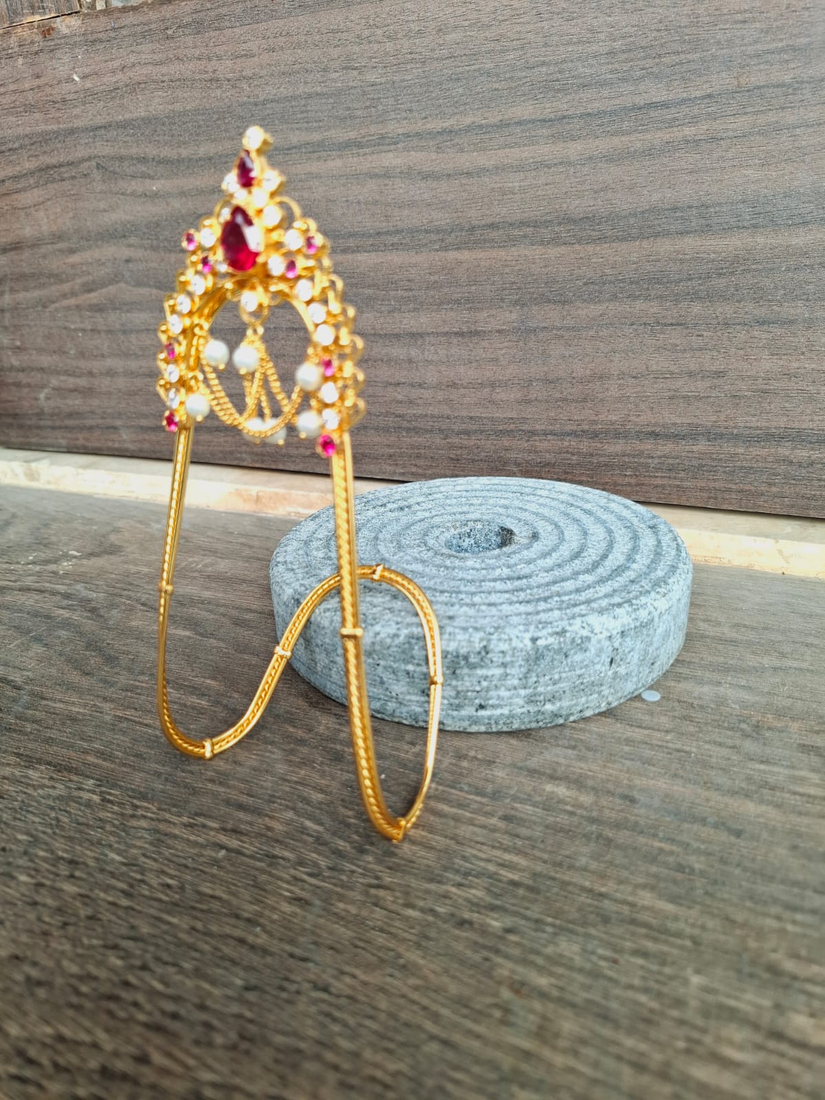 Ornate gold-tone jewelry piece with colorful stones, displayed on a wooden surface next to a coiled gray rope.