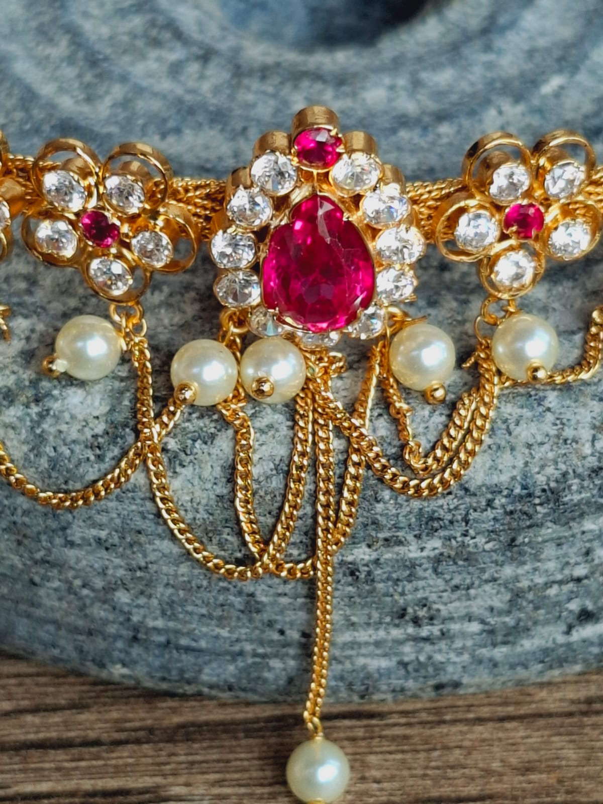 Ornate gold-toned Chatai Flower Oval Chocker cum Bajuband with vibrant red gems and glittering white stones, accented by delicate pearl details, displayed on a gray background.