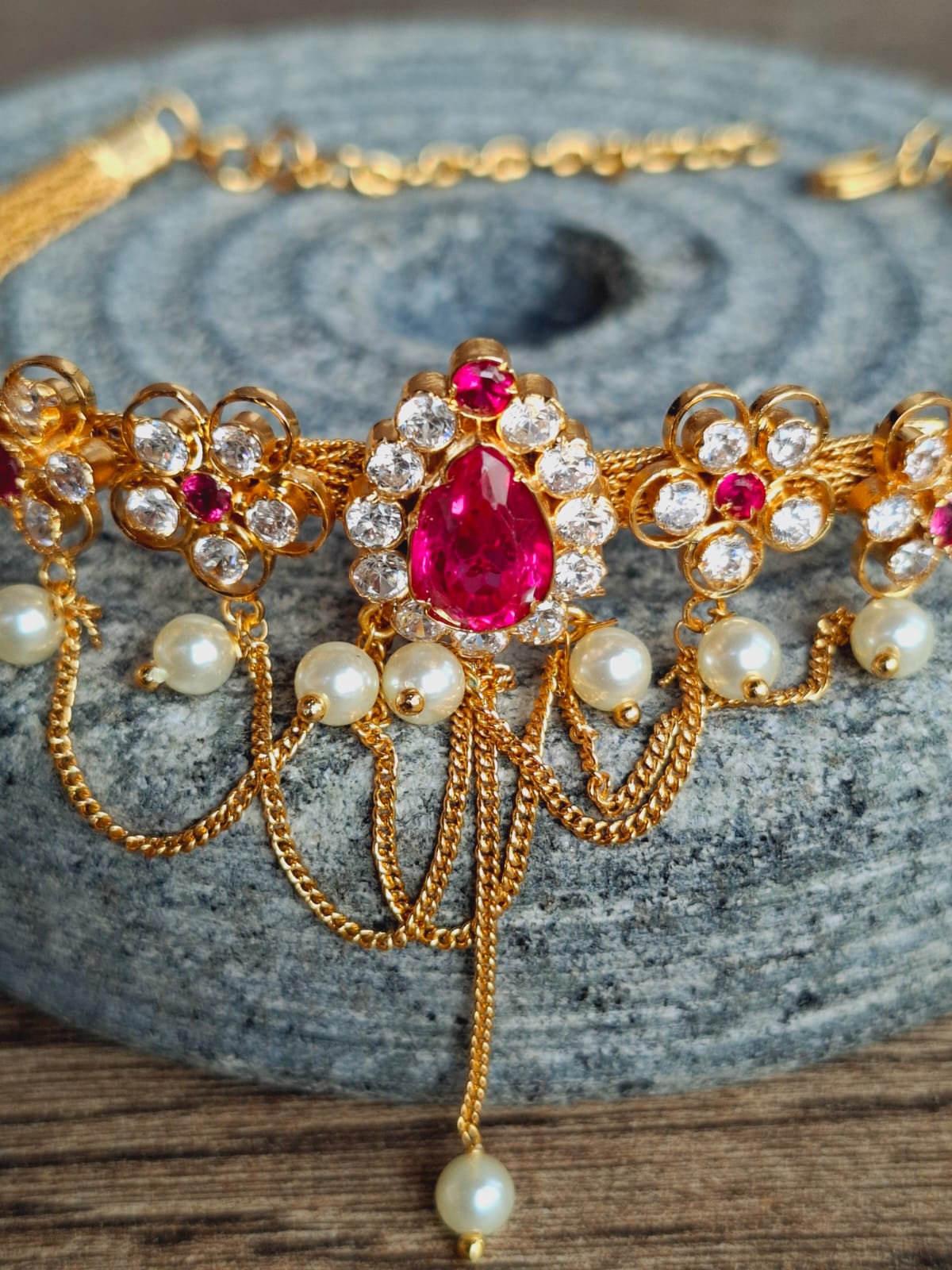 Ornate gold floral choker necklace with red gemstones and pearl accents displayed on a grey surface.