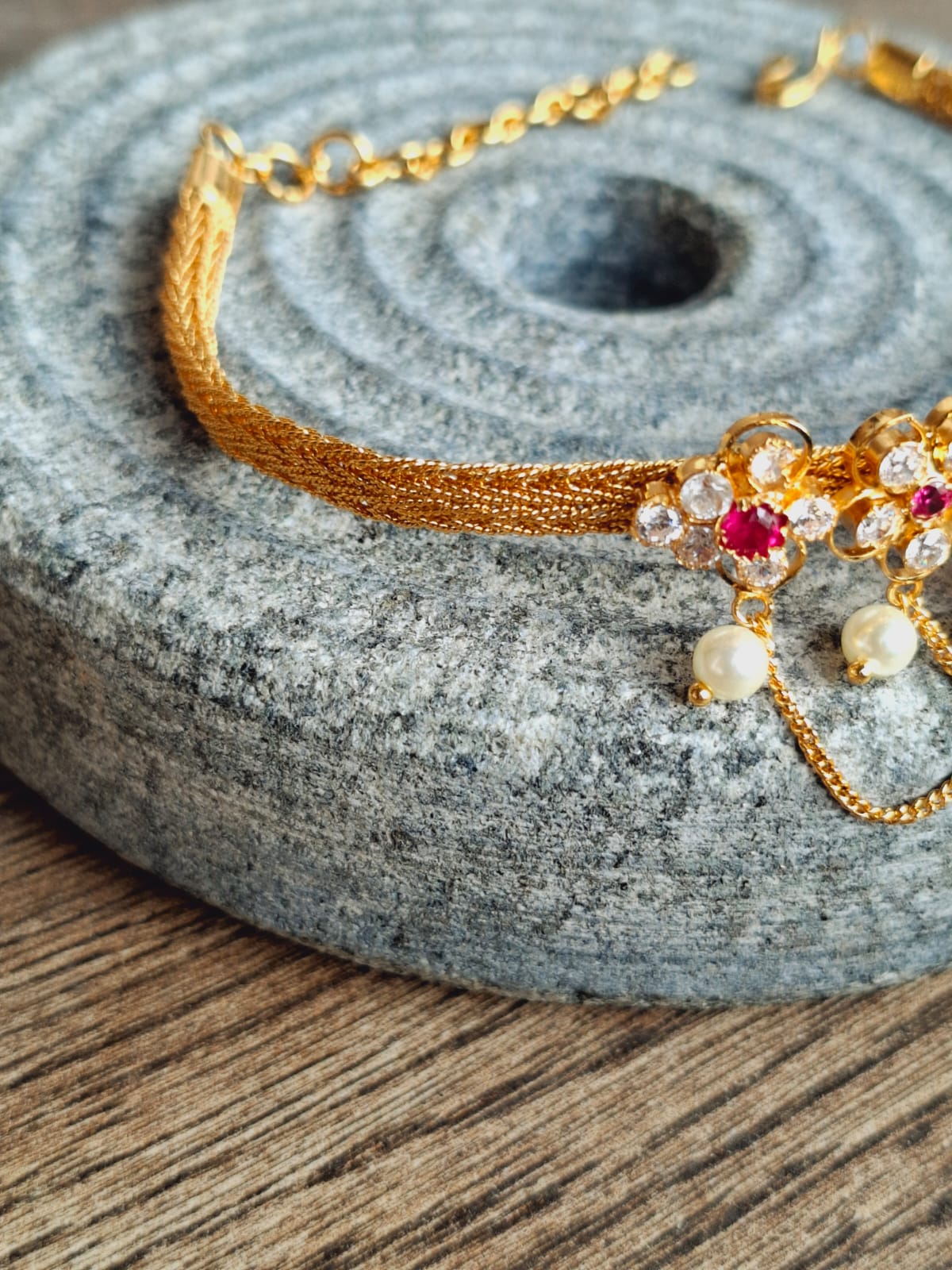 Intricate gold choker necklace with floral pendant and pearl accents, placed on a grey stone surface.