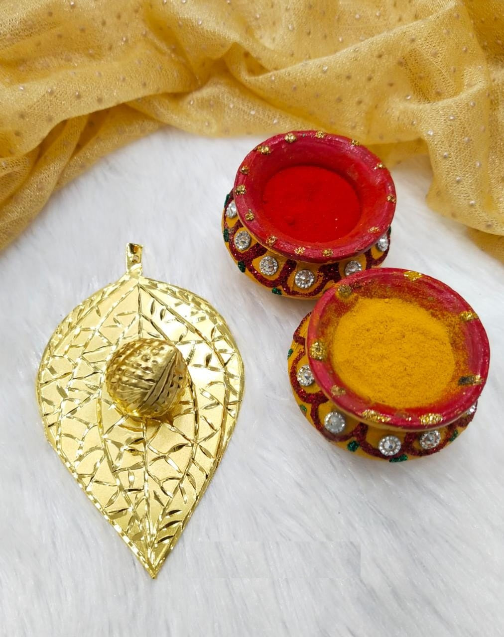 Decorative golden leaf-shaped pendant and two red and gold painted trinket dishes on a white surface with a shimmering golden fabric in the background.