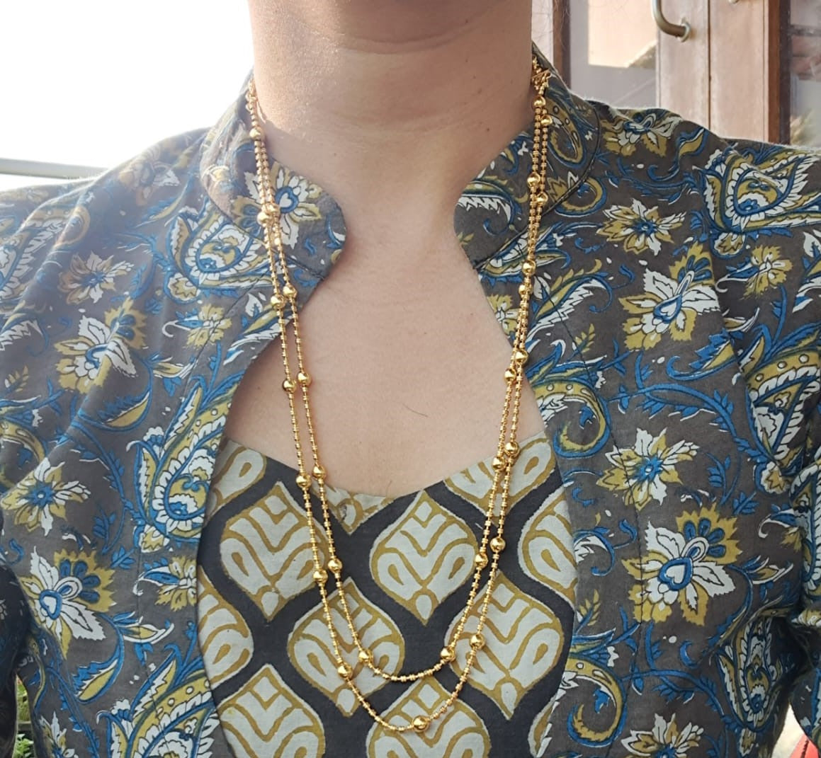 Ornate gold necklace with lyre-shaped pendants, displayed on a model wearing a vibrant floral-patterned blouse
