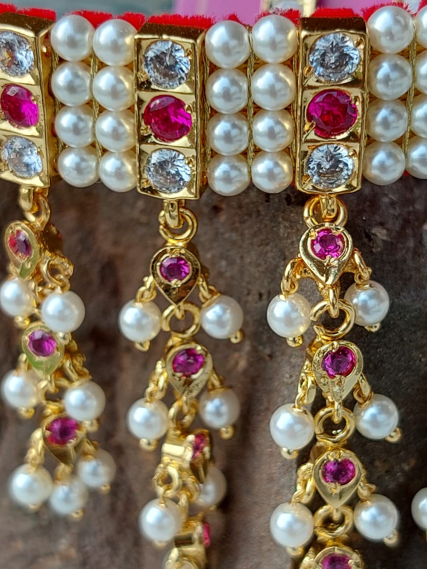 Gold-toned jewelry set with pink and white gemstones, featuring pearls, crystal embellishments, and dangling elements. The product is placed against a dark background, highlighting the intricate design and luxurious appearance of the jewelry item.