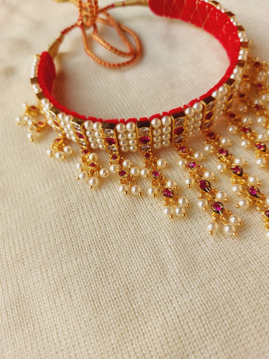 Ornate golden and red beaded necklace with hanging pearl and bead details, displayed on a light textured background.