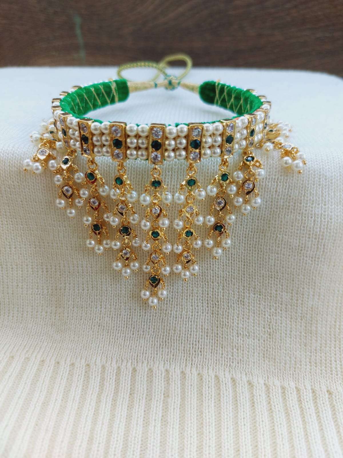 Elegant beaded necklace with green and golden pearls, featuring a cascading fringe design, showcased on a white fabric background in the Mugdha Jewellery Store product image.