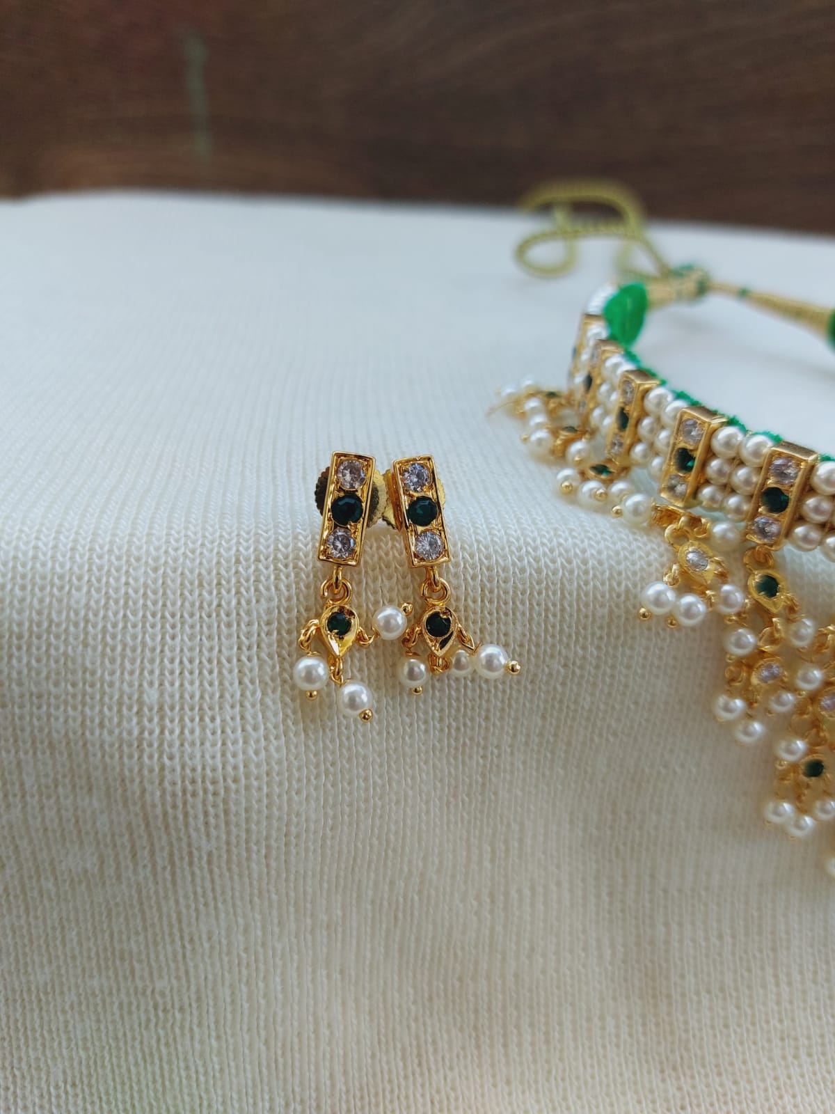 Elegant gold-toned earrings with intricate beading and pearls, resting on a soft white fabric backdrop.