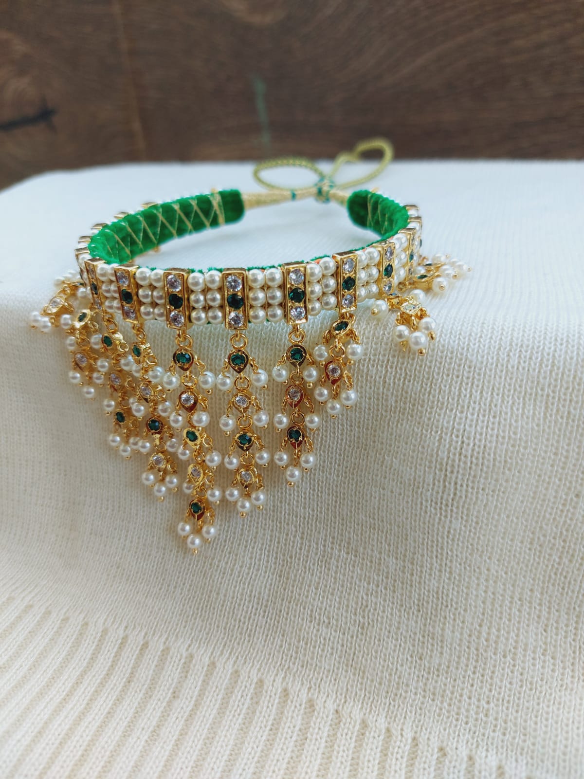 Elegant 15 Patti green and white gadi zhalar chinchpeti with sparkling crystals and pearls on a white background.