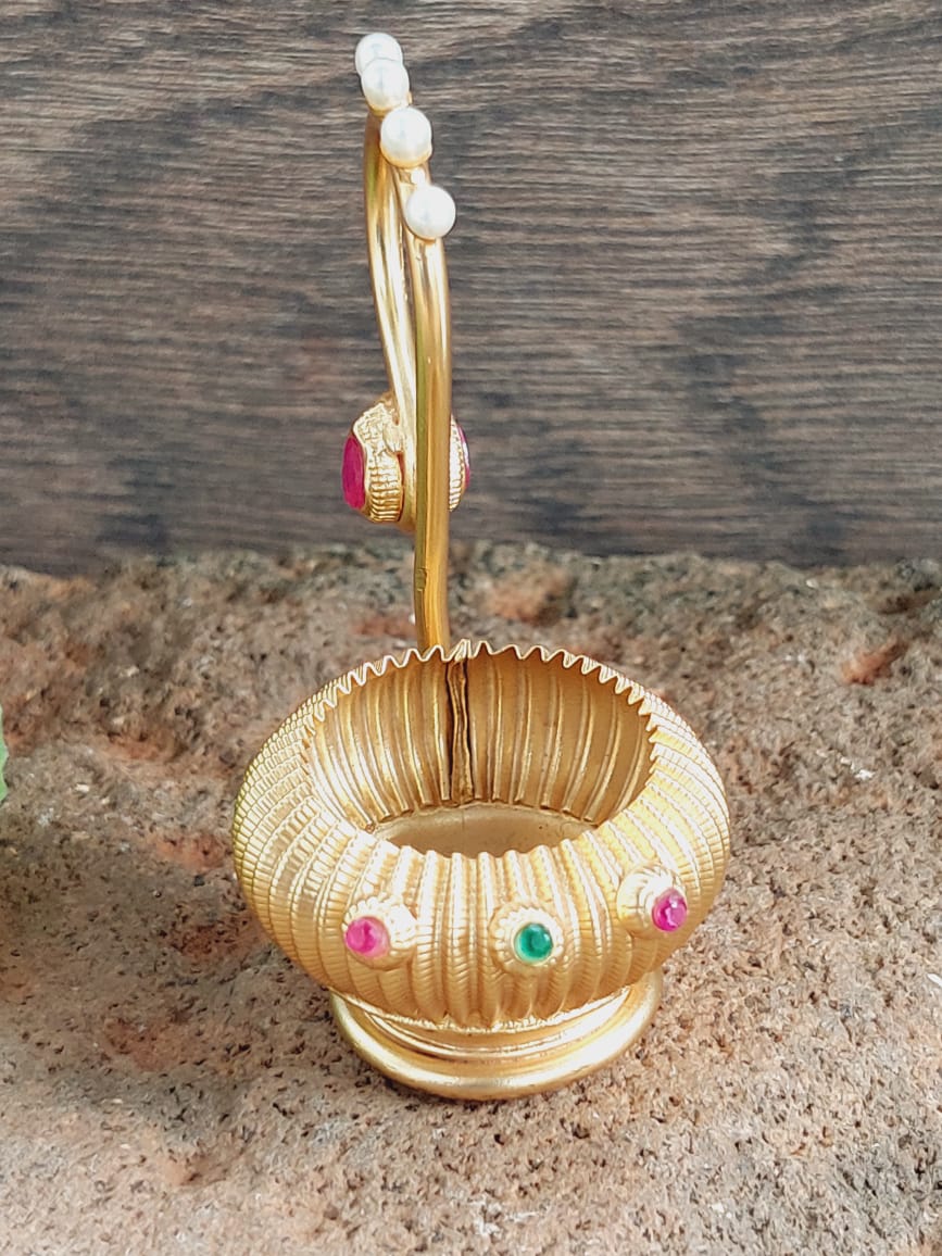 Gold-toned decorative Haldi Kumkum Karanda container with colored stones and pearls on a wooden surface