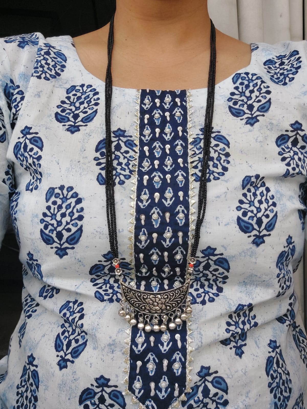 Ornate Designer Chandrakor Oxidised Long Mangalsutra on model wearing printed blue and white dress showcasing the statement jewelry piece.