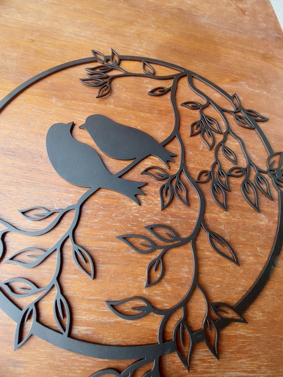 Beautiful Bird Mild Steel Wall Decor - A black metal bird silhouette perched on a leafy branch against a warm wooden background.