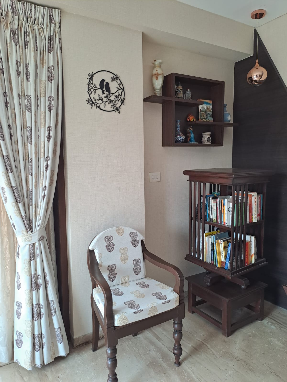 Decorative metal bird wall art in a cozy living room setting with a patterned armchair, wooden bookshelf, and hanging lighting fixture.
