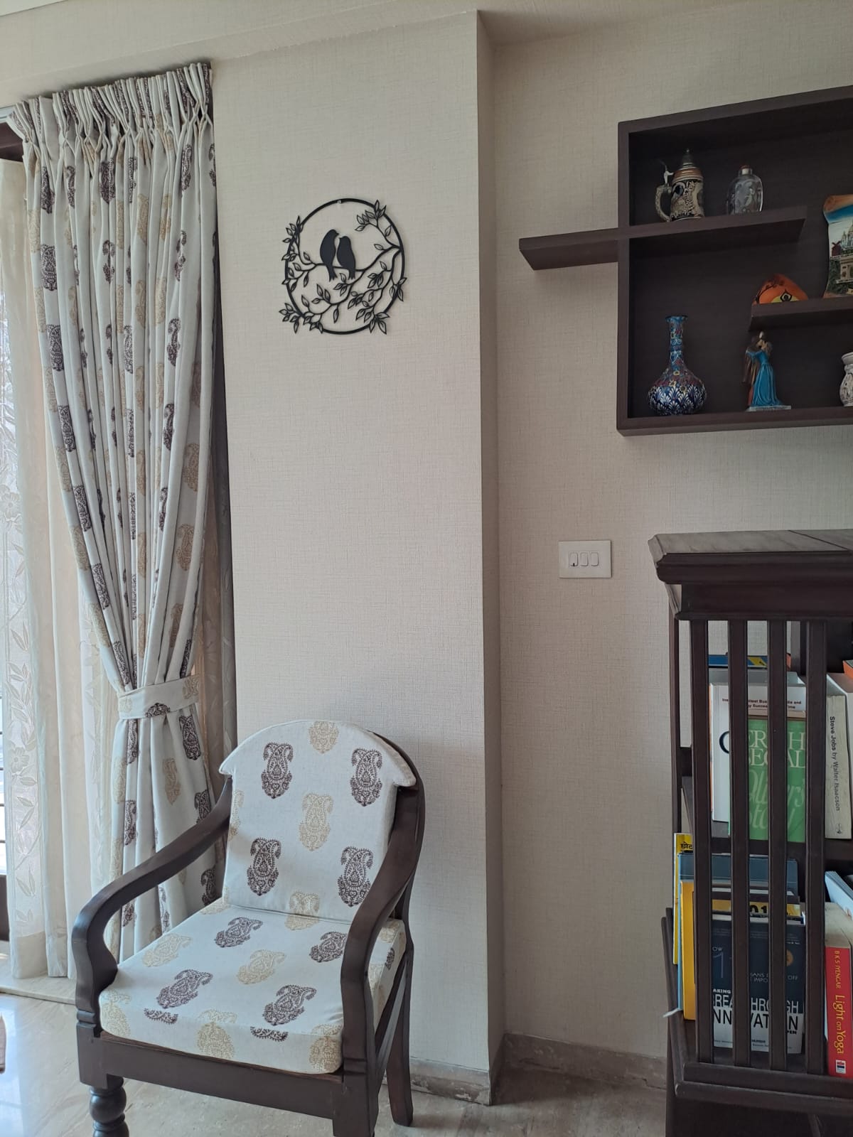 Decorative bird-shaped metal wall art, wooden shelving unit with trinkets, and a patterned armchair in a cozy home interior setting.
