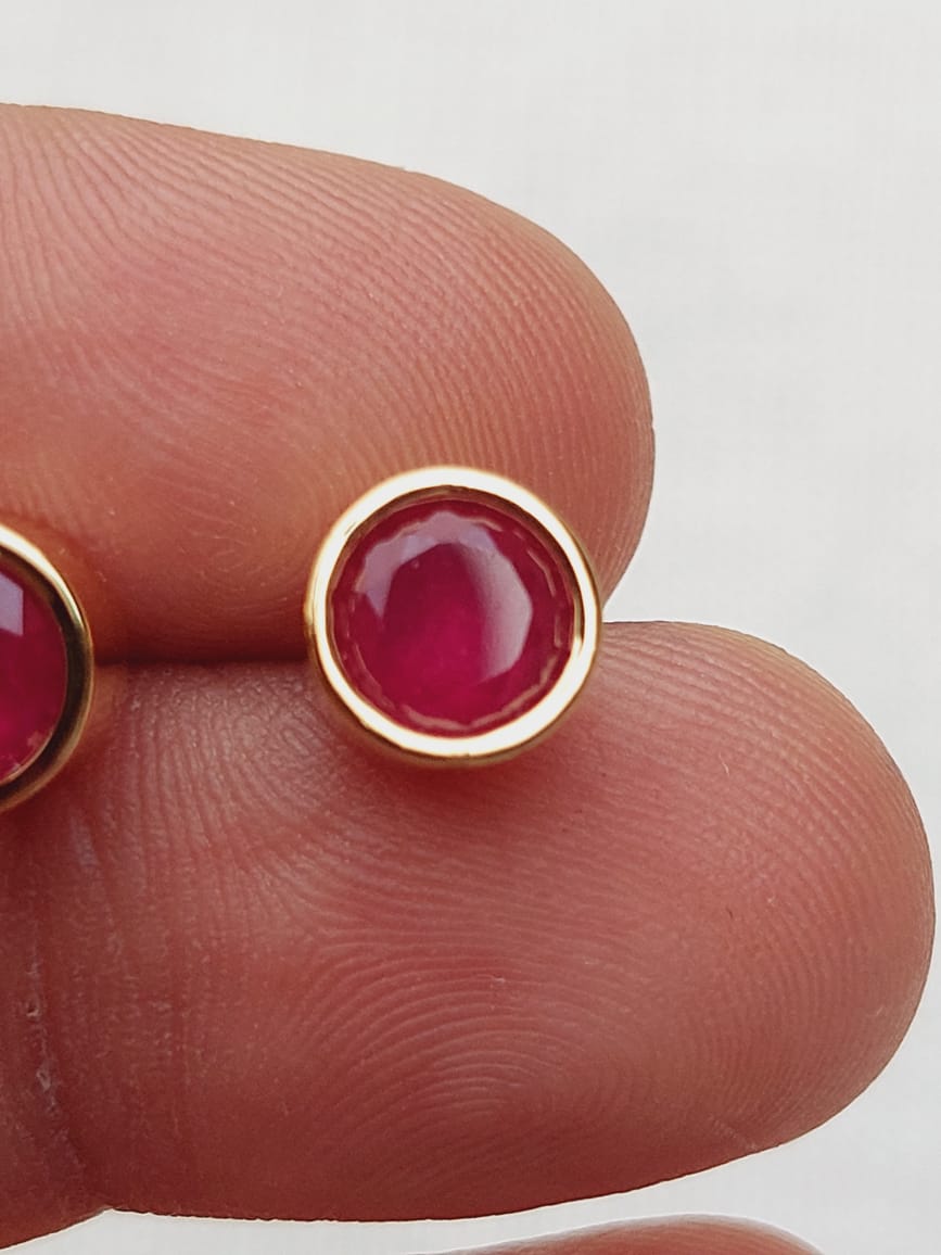 Elegant small red studs against finger tips, showcasing the Mugdha Jewellery Store brand.