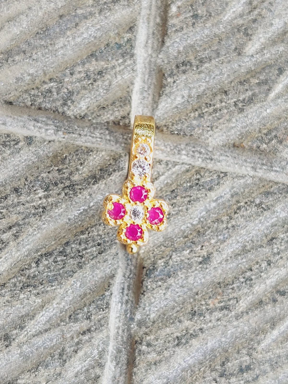 Red Flower Nose Pin - Captivating golden nose accessory adorned with vibrant red floral gems, showcased against a textured grey background.