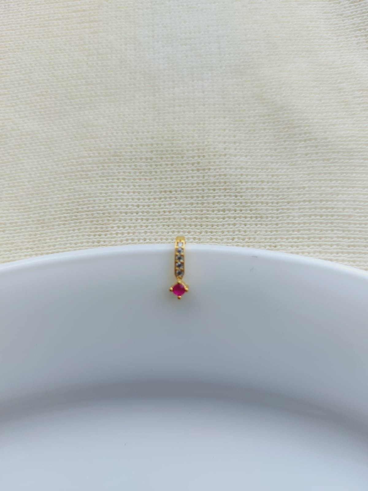Elegant Red Stone Nose Pin - A delicate gold-toned nose pin adorned with a captivating red stone, showcased on a white background.