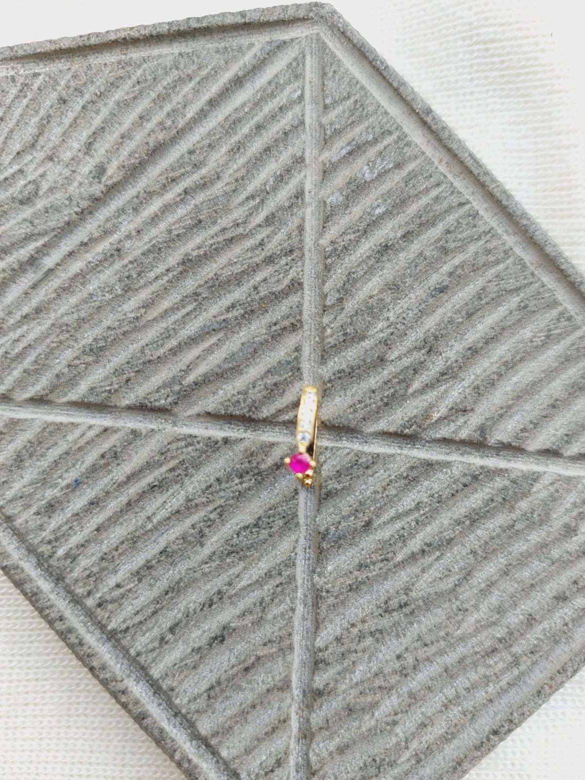 Delicate Red Stone Nose Pin - A decorative nose accessory featuring a small red stone, elegantly displayed against a textured gray background.