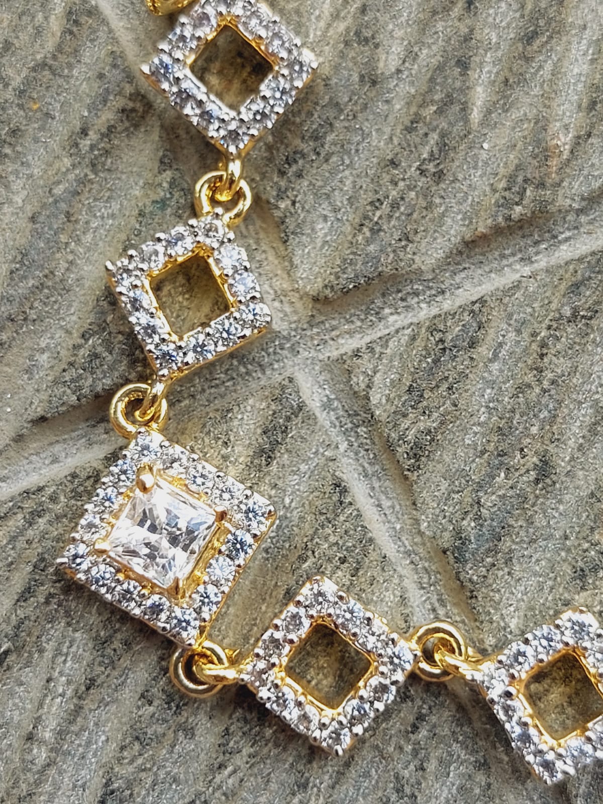 Elegant diamond-encrusted bracelet with adjustable gold-toned links and a central diamond-shaped pendant, resting on a natural stone surface.