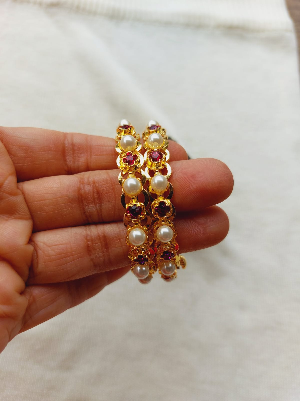 Elegant gold-toned earrings with clustered yellow and red gemstones and white pearls, showcased in a hand-held display.