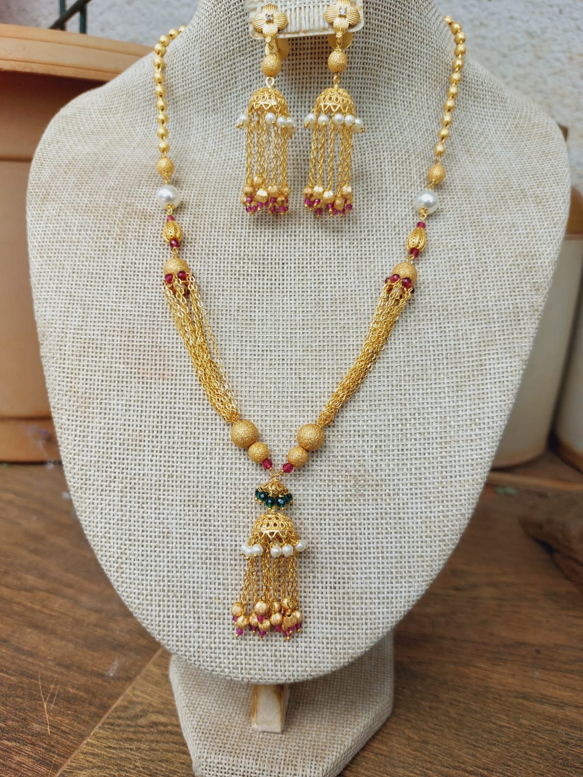 Elegant gold-toned designer jewelry set featuring a necklace with a pendant and matching earrings, displayed on a white textile background.