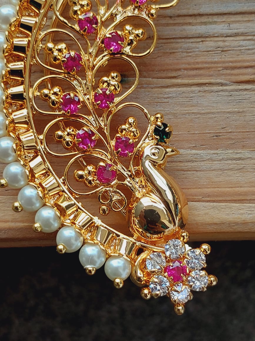 Ornate golden jewelry with intricate floral patterns, studded with sparkling pink gemstones and pearls, displayed on a wooden background.