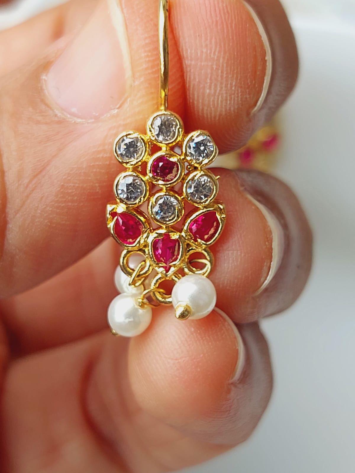 Sparkling gold flower-shaped earring with ruby and diamond accents, held in a hand against a plain background.