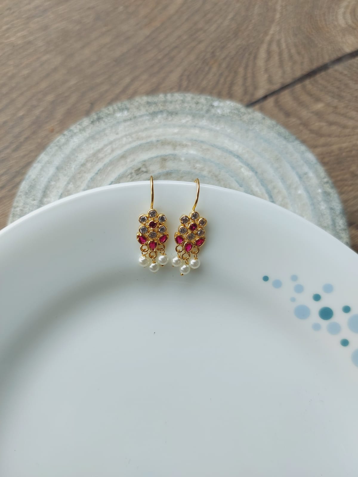 Elegant pink and white floral earrings showcased on a white ceramic plate atop a wooden background.