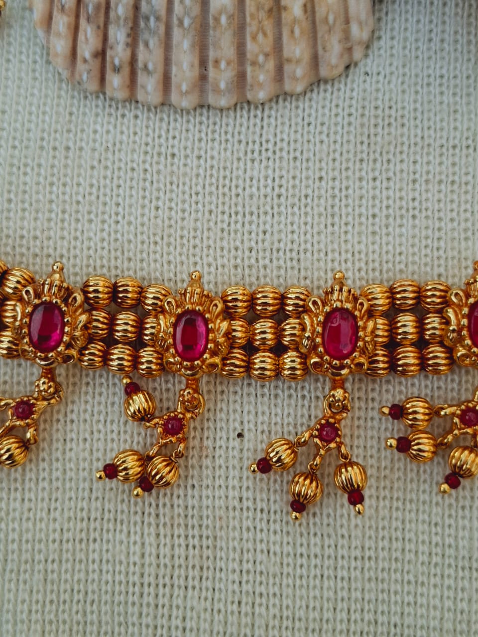 Elegant gold-toned antique chinchapeti necklace with intricate ruby-colored gemstone accents, showcased on a knitted textured background.