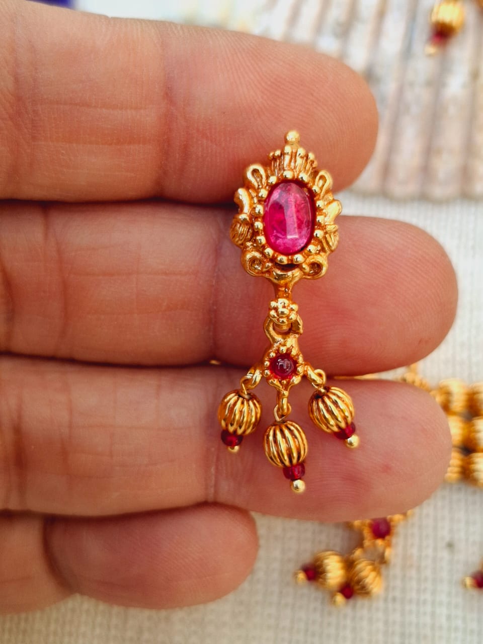 9 Patti Designer Antique Chinchapeti
Exquisite gold-toned pendant with a vibrant red oval-shaped gemstone, adorned with delicate floral motifs and dangling embellishments.