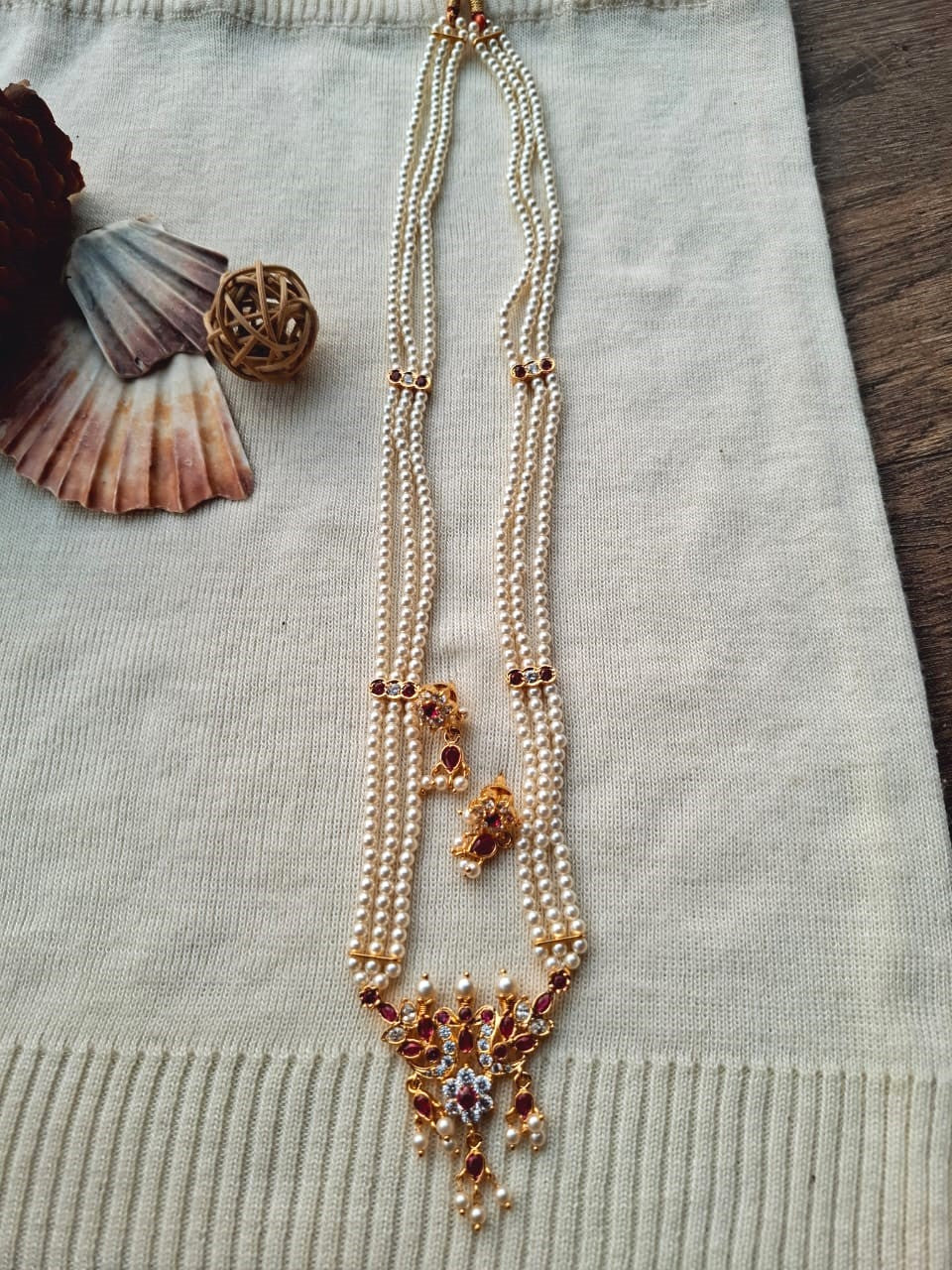 Ornate golden pearl necklace with intricate peacock pendant and beaded tassels, displayed on a white fabric background.