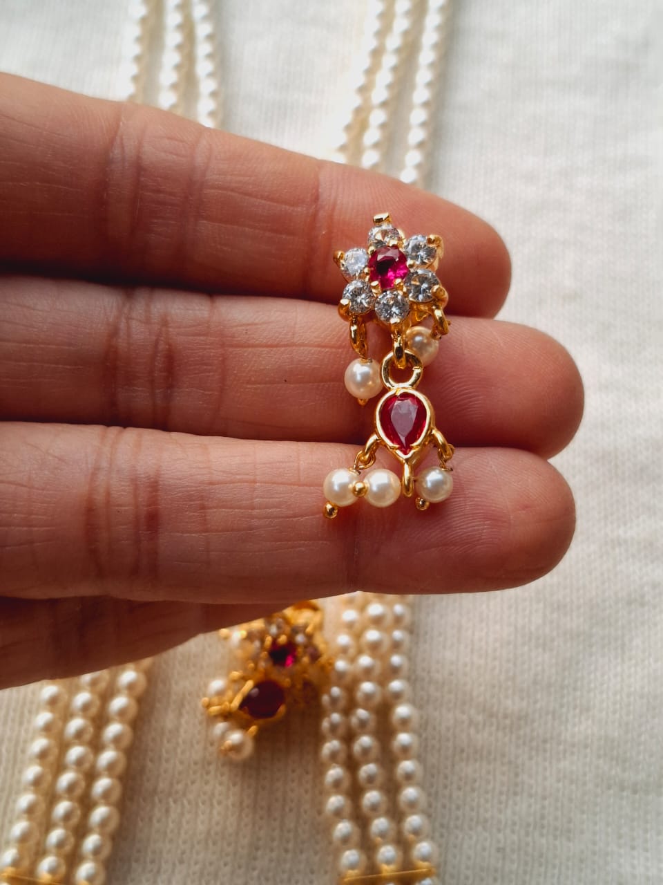 Elegant gold-toned pendant with gemstone and pearl accents, displayed on a string of pearls in the Mugdha Jewellery Store product image.